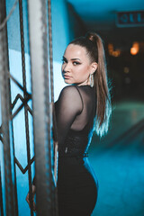 Poster - Pretty Caucasian lady with black overalls posing in the parking with blue LED lights