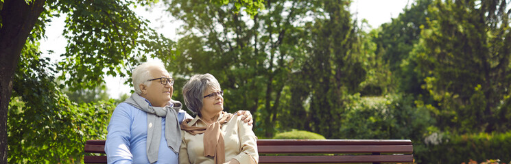 An elderly couple man and women of Asian incursion, happily spend time in a city park, sit on a bench hugging and smiling, the concept of a long happy family life.