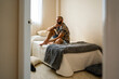 © Eloisa Ramos/Stocksy - Hipster man looking the window on the bed