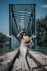 Poster - Young Caucasian girl in a long evening dress posing on a bridge with her hand on her forehead