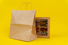 Dog Treats Made Of Dried Meat In Cardboard Box With Transparent Cover, Tied With Twine, Stands With An Eco-friendly Package On A Yellow Background, Front View, Copy Space.