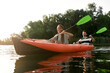 © Svitlana - Couple of young adventurous explorers looking cheerful while kayaking in a river surrounded by the beautiful nature on a summer day