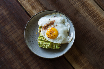 Wall Mural - Top view of a healthy breakfast plate of fresh avocado toast with a fried egg on a wooden table