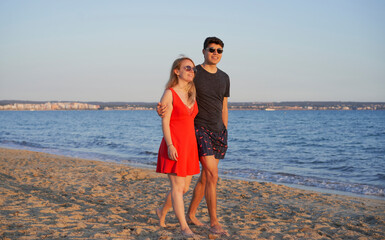 Couple of cheerful multiracial friends, embracing walking on the beach of Can Pastilla, celebrating, having fun during summer holidays. Celebration concept