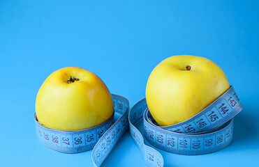 Two yellow apples wrapped in a centimeter tape. Concept of healthy and proper nutrition, diet, weight loss. Side view. Copy space, selective focus.