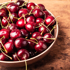 Plate with ripe red, juicy cherries on a wooden table, close-up