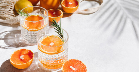 Summer orange cocktails with fresh citrus fruits. Hard seltzer, lemonade, refreshing drinks, low alcohol mocktails, summer party concept. Shadow and sunlight. Banner, flat lay, top view, copy space.