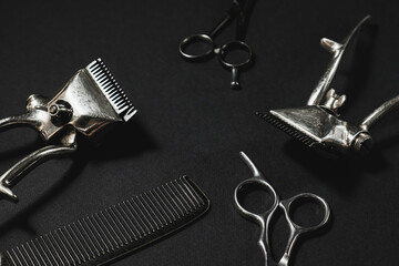 On a black surface are old barber tools. two vintage manual hair clipper, comb, hairdressing scissors. black monochrome. contrast shadows. horizontal .