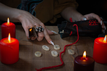 Wall Mural - A woman's hand with rings pointing to runes lying on a wooden table surrounded by burning candles on a dark background I am selective focus