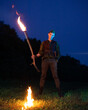 © ISliM - A guy dressed as Peter Pan stands with a burning torch against the night sky and dark forest