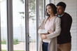 © Wavebreak Media - Thoughtful hispanic couple standing at window looking out and embracing