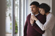 © Wavebreak Media - Thoughtful hispanic couple standing at window looking out and embracing