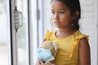 © Wavebreak Media - Sad hispanic girl standing at window looking out of window holding teddy bear in face mask