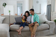 © Wavebreak Media - Smiling hispanic mother, father and daughter sitting on couch using laptop together