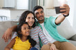 © Wavebreak Media - Smiling hispanic mother, father and daughter sitting on couch taking selfie together