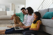 © Wavebreak Media - Smiling hispanic mother, father and daughter sitting on living room floor using laptop together