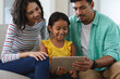 © Wavebreak Media - Smiling hispanic mother, father and daughter sitting on couch using tablet together