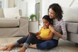 © Wavebreak Media - Smiling hispanic mother and daughter sitting on living room floor using tablet together