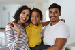 © Wavebreak Media - Portrait of smiling hispanic father embracing with wife and daughter standing in living room