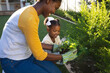 © Wavebreak Media - Happy african american mother and daughter kneeling tending to plants in sunny garden