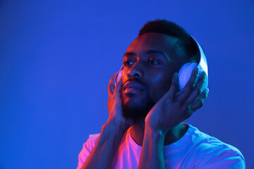 African-american young man's portrait on dark studio background in neon. Concept of human emotions, facial expression, youth, sales, ad.