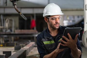 Wall Mural - Male automation engineer using tablet control robot arm welding machine in an industrial factory.Artificial intelligence