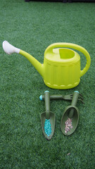 Sticker - Closeup shot of a small plastic watering can and shovels with colored seeds in a garden