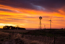 Windmill And Wind Turbines Silhouetted Against Sunset