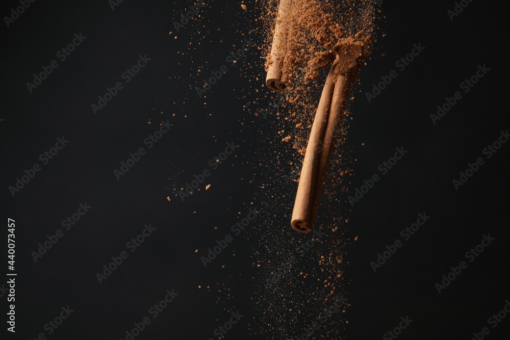 Falling cinnamon sticks and powder on dark background