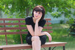 © ALEXEY - Portrait of a happy young woman in black dress on a bench in the park.