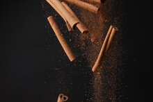 Falling Cinnamon Sticks And Powder On Dark Background