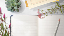 白木のテーブルの上にある空白のノートブック、鉛筆、鉢植えの植物、切り花。ナチュラルなインテリアの背景テクスチャー。