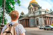 A young blond man stands on the street and looks at St. Isaac's Cathedral in Saint Petersburg, a popular tourist attraction