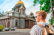 A young blond man stands on the street and looks at St. Isaac's Cathedral in Saint Petersburg, a popular tourist attraction