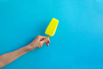 Child hand holding yellow ice cream popsicle on blue color background