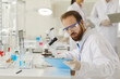 © Studio Romantic - Medical male pharmacy scientist wearing protective clothes and goggles working in laboratory comparing test sample reading paper report on clipboard sitting at desk. Medicine and biotech