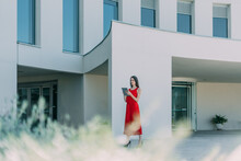 Young Business Woman In Red Dress And Typing On Her Tablet At The Entrance To The Office.