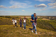 © Studio Romantic - Hiking and traveling concept. Group of young friends hikers tourists traveling with backpacks on nature in row together with green valley landscape at background during summer vacations on sunny day
