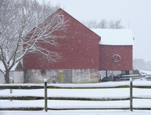 A Architectural Gem Of A Red Barn With A Green Wreath Photographed During A Christmas Time Snowstorm