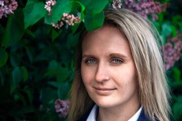 Portrait of a young beautiful blonde on a background with bushes with lilacs.