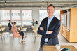 © Annika List/Westend61 - Smiling businessman standing with arms crossed at conference centre