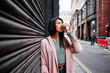 © Angel Santana Garcia/Westend61 - Beautiful woman in overcoat drinking coffee while standing by closed shutter in city