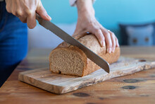 Woman cutting loaf of bread on cutting board at home