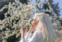 Mature Woman With Long White Hair Smelling Flowers On Sunny Day