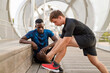 © Ignacio Ferrandiz Roig/Westend61 - Young man looking while friend tying shoelace on wooden seat