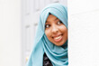 © Ignacio Ferrandiz Roig/Westend61 - Smiling woman wearing hijab peeking around wall