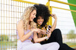 © Jose Carlos Ichiro/Westend61 - Laughing female friends looking at smart phone while sitting by fence