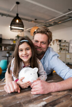 Smiling Father And Daughter With Piggy Bank At Home