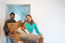 Smiling young couple carrying cardboard boxes while standing at doorway