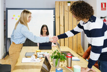 Blond Female Professional Greeting Colleague At Board Room In Office